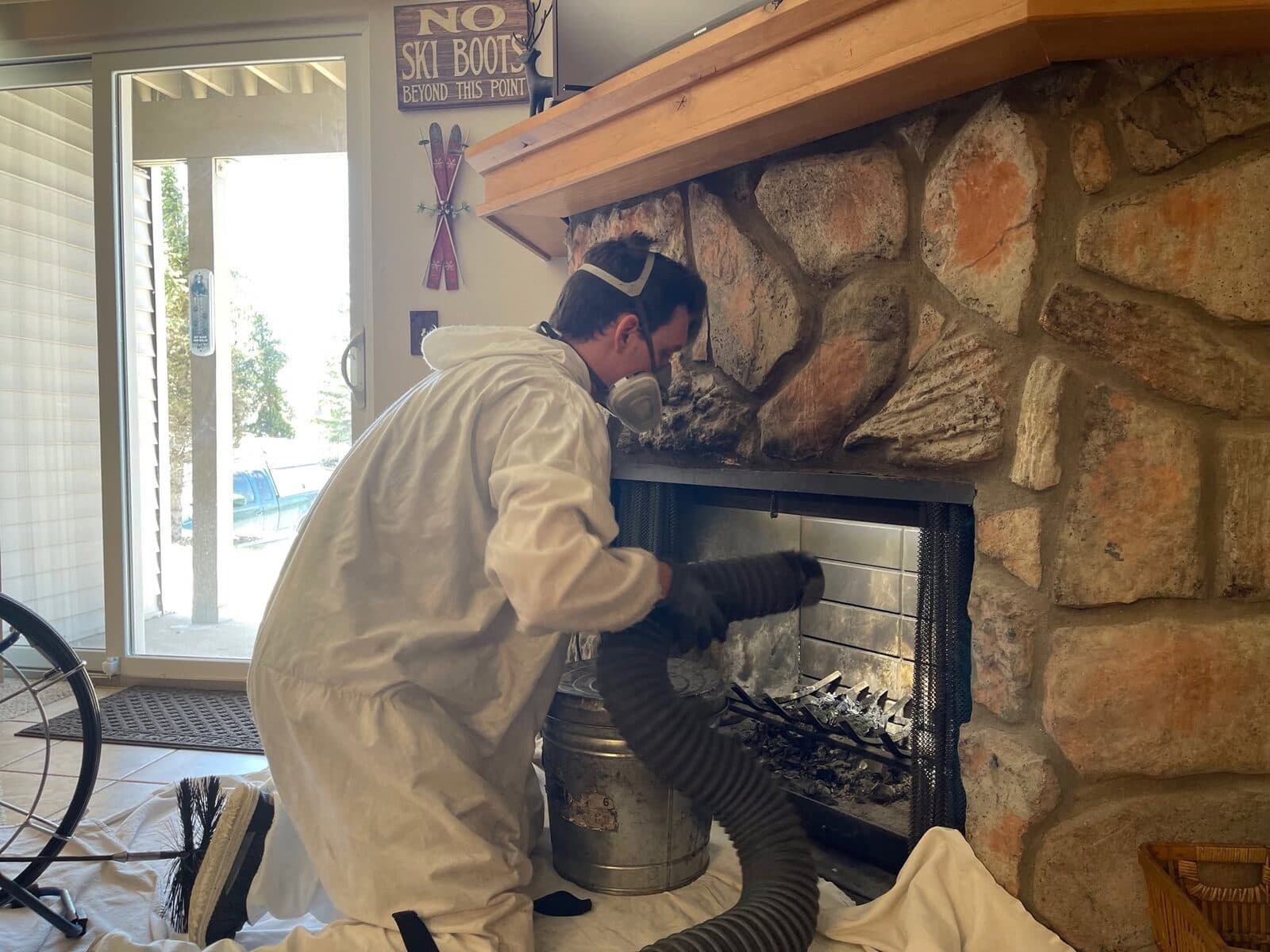 Technician in protective gear working at a fireplace insert with HEPA vacuum